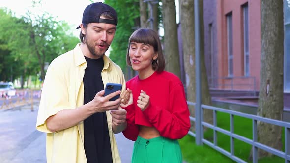 Happy Millenial Couple Dancing From Happiness Looking To Phone on Street