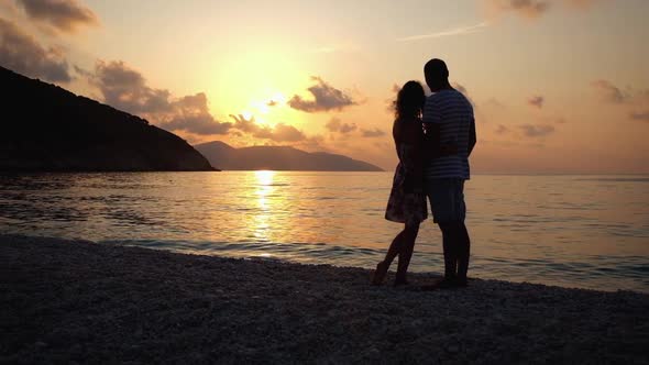 Couple in love hugging each other standing on the beach at sunset
