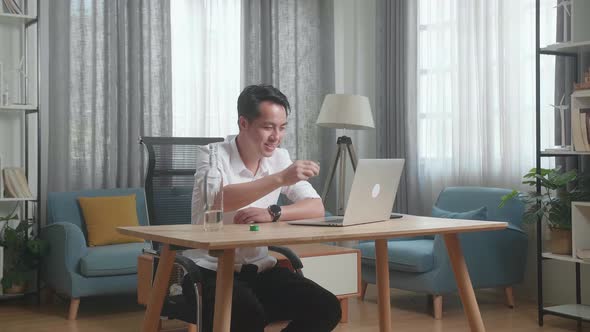 Smiling Asian Man Drinking Vodka During Having Video Call On A Laptop At The Home