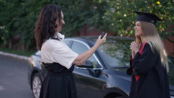 Loving Mature Mother Giving Car Keys to Excited Graduated Daughter Outdoors