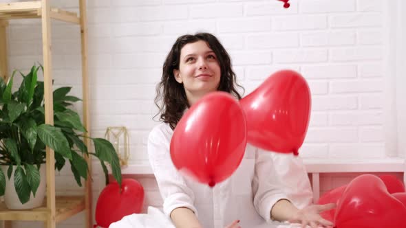 Brunette European Girl Rejoices Playing on Bed with Red Heart Shape Balloons