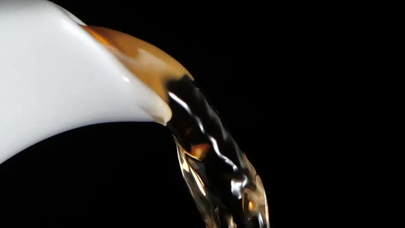 Tea Stream Pouring From Ceramic Teapot. Black Background, Slow Motion