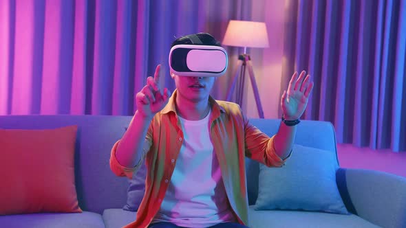 Asian Man Wearing Vr Headset At Living Room, Using Hand Touching And Slide, Cyan And Magenta Colors