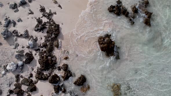 Low Aerial, drone shot of a white beach with rocks and small waves washing ashore at the outer reef