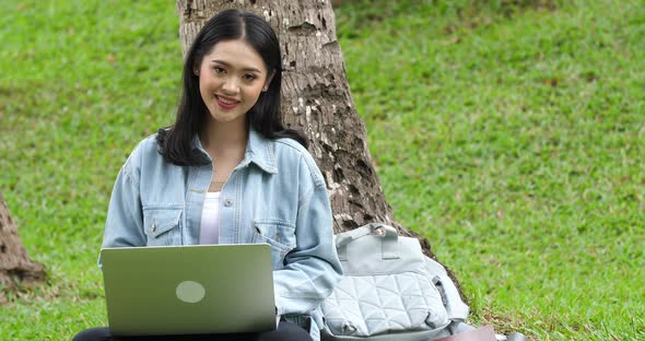 Female Student Sitting On Grass With Laptop Computer And Looking At Camera