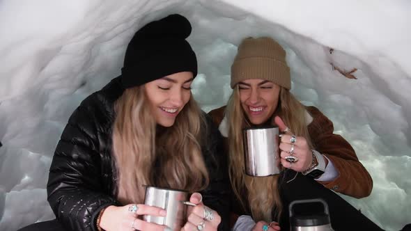 Twin sisters cheering with mugs while in igloo