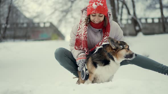 Happy Young Woman Walking with Her Welsh Corgi Dog in Snowy Winter Park