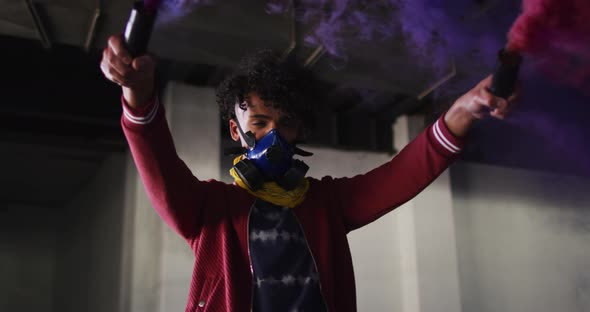 Mixed race man holding blue and purple flares standing in an empty building