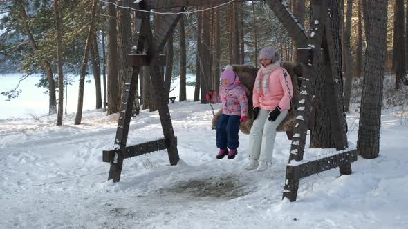 Woman with Child Swinging on Swing in Winter Day