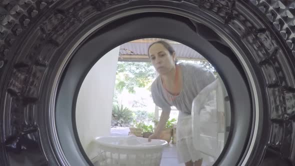 A GoPro view from inside a washing machine of a woman putting in dirty clothes