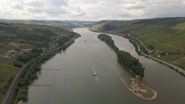 Long cargo ship traveling along the rhine river between lush meadows and vineyards on a sunny day. H