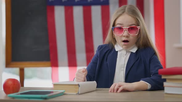 Amazed Schoolgirl with Surprised Facial Expression Looking at Camera Sitting on the Right in School