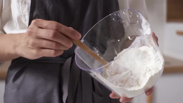 Plastic Glass With Flour. Woman Pours Flour Wooden Ladle To Make Dough. Glass Bowl Of Wheat Flour