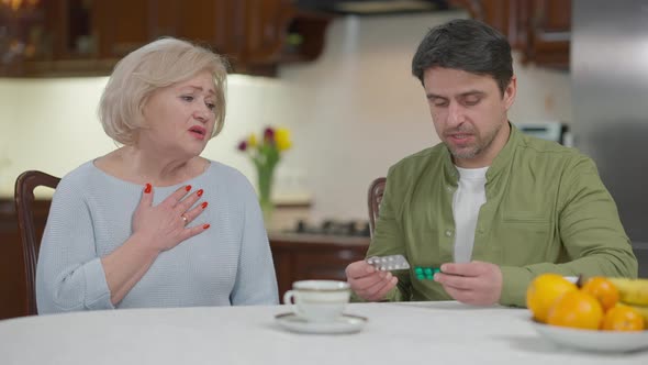 Confident Adult Son Taking Care of Ill Senior Mother Talking Explaining Pills Administration