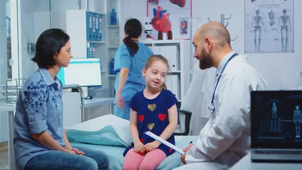 Doctor Talking with Little Girl Sitting on Bed