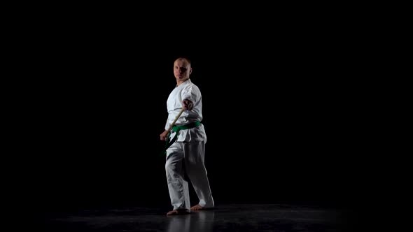 Kendo Fighter on White Kimono Practicing Martial Art with the Bamboo Bokken on Black Background