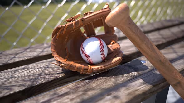 Baseball mitt with ball and bat at a wooden bench. Sports gear. American sport.