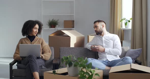 Happy Afro American Woman Browses Laptop in New Flat Caucasian Man Looks at Smartphone Screen Move