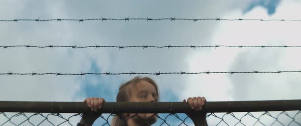 Young woman climbs metal fence and she is looking around over the fence