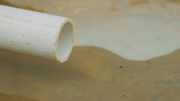 Water slowly dripping on a concrete floor from a white PVC pipe making a puddle - Close up