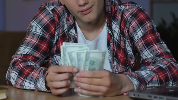 Handsome Teenager Counting Dollar Bills, Sitting at Table, Dreaming Purchase