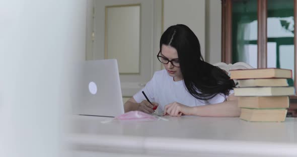 Diligent Girl in Glasses Studying Noting and Typing on Laptop at Table in Room