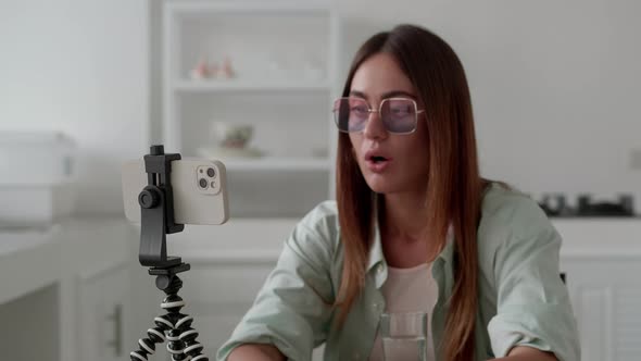 Young Female Blogger Look Smartphone on Tripod and Say Wow on Modern Interior Background