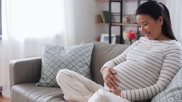 Happy Pregnant Asian Woman Sitting on Sofa at Home