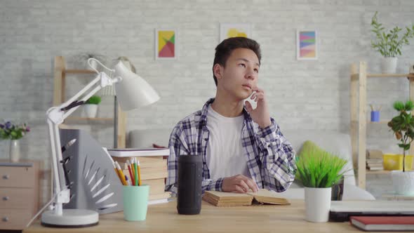 Young Asian Man in a Shirt Reads a Book and Uses a Voice Assistant