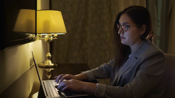 Tired Woman Typing on a Laptop By the Light of a Table Lamp