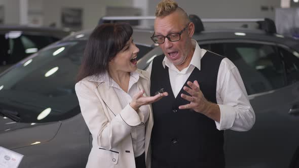 Front View Portrait of Excited Caucasian Adult Couple Posing with Car Key in Dealership Looking at