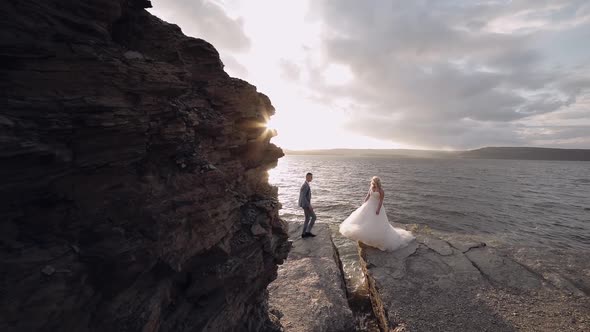 Groom Goes To Bride and Gives Her a Hand. Newlyweds on Mountainside By the Sea