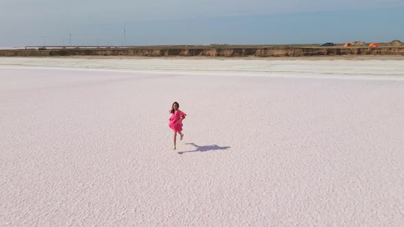 Aerial Drone Shot of Beautiful Joyful Woman in Pink Dress Jogging and Running Across Salt Flats of
