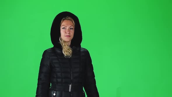 Blonde Girl in a Black Winter Coat with Hood Going Against a Green Screen. Slow Motion