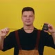 Young Handsome Builder Holds a Tape Measure Ruler in His Hands on a Yellow Background - VideoHive Item for Sale