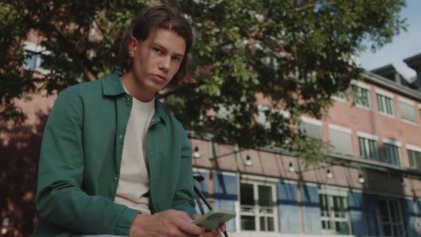 Young Guy Sitting Outdoors and Using Modern Smartphone