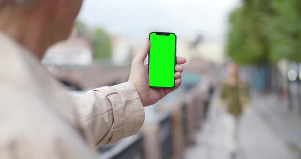 View Over Shoulder of Mature Man Holding Cellphone with Blank Green Screen in City