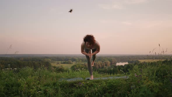 A Young Woman Keeps Her Balance By Doing Yoga Exercises on a Carpet in Nature in the Background a