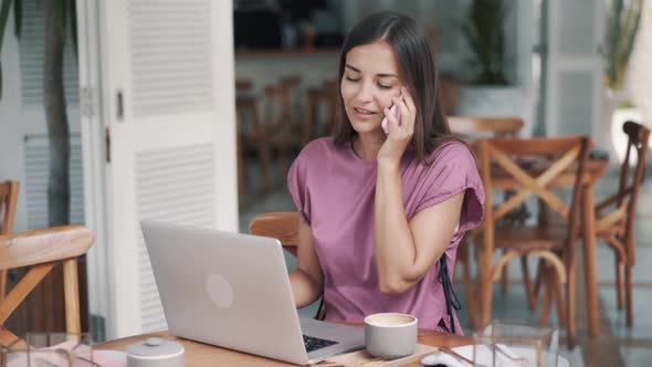 Woman Freelancer in Cafe Uses Laptop for Work, Talking on Phone, Drinking Coffee