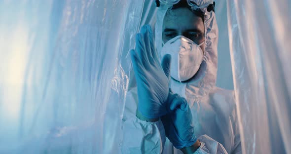 Male doctor puts on blue gloves over a plastic curtain