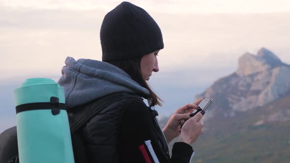 Young Girl Traveler with Backpack Using Smartphone Digital Device Blurred Top Mountain Background