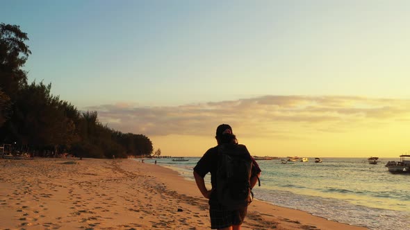 Backpacker girl walking around exotic beach at sunset with warm colors on dusty sky, alongside seash