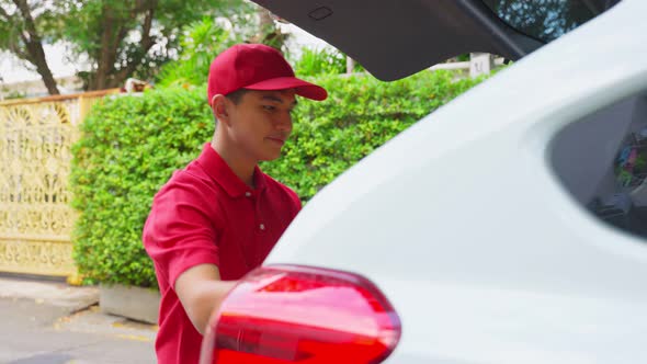 Asian deliver man wearing face mask in red uniform handling bag of food, groceries, fruit from car.