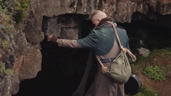 Man In Long Coat With Guitar Case Walking Into Cave