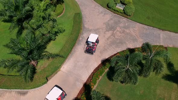 Aerial top down shot following two golf carts on path between green golf course