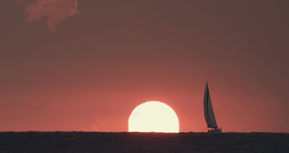 Sunset over the sea with a sail boat silhouette, super telephoto footage