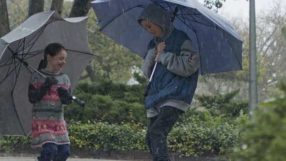 Boy and a girl jumping with umbrellas in the pouring rain in slow motion