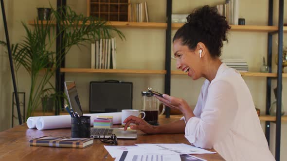 Mixed race woman using laptop and talking on smartphone while working from home