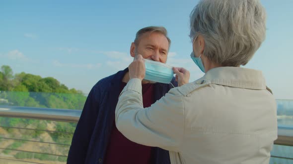 Elderly Woman Putting on Medical Mask on Bearded Husbands Face