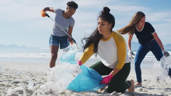 Diverse group of female friends putting rubbish in refuse sacks at the beach